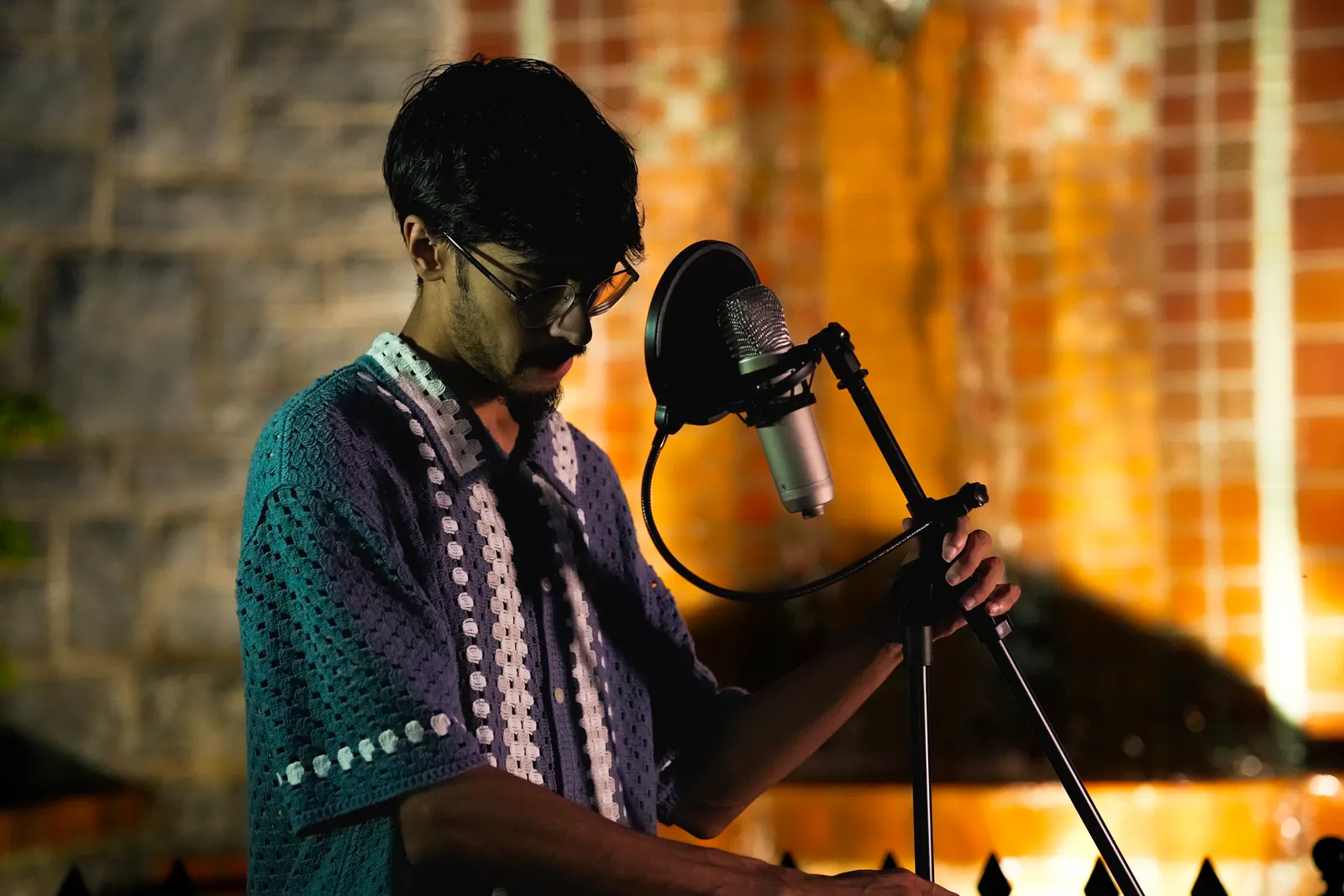 A vocalist in a knit shirt adjusting a microphone stand at night