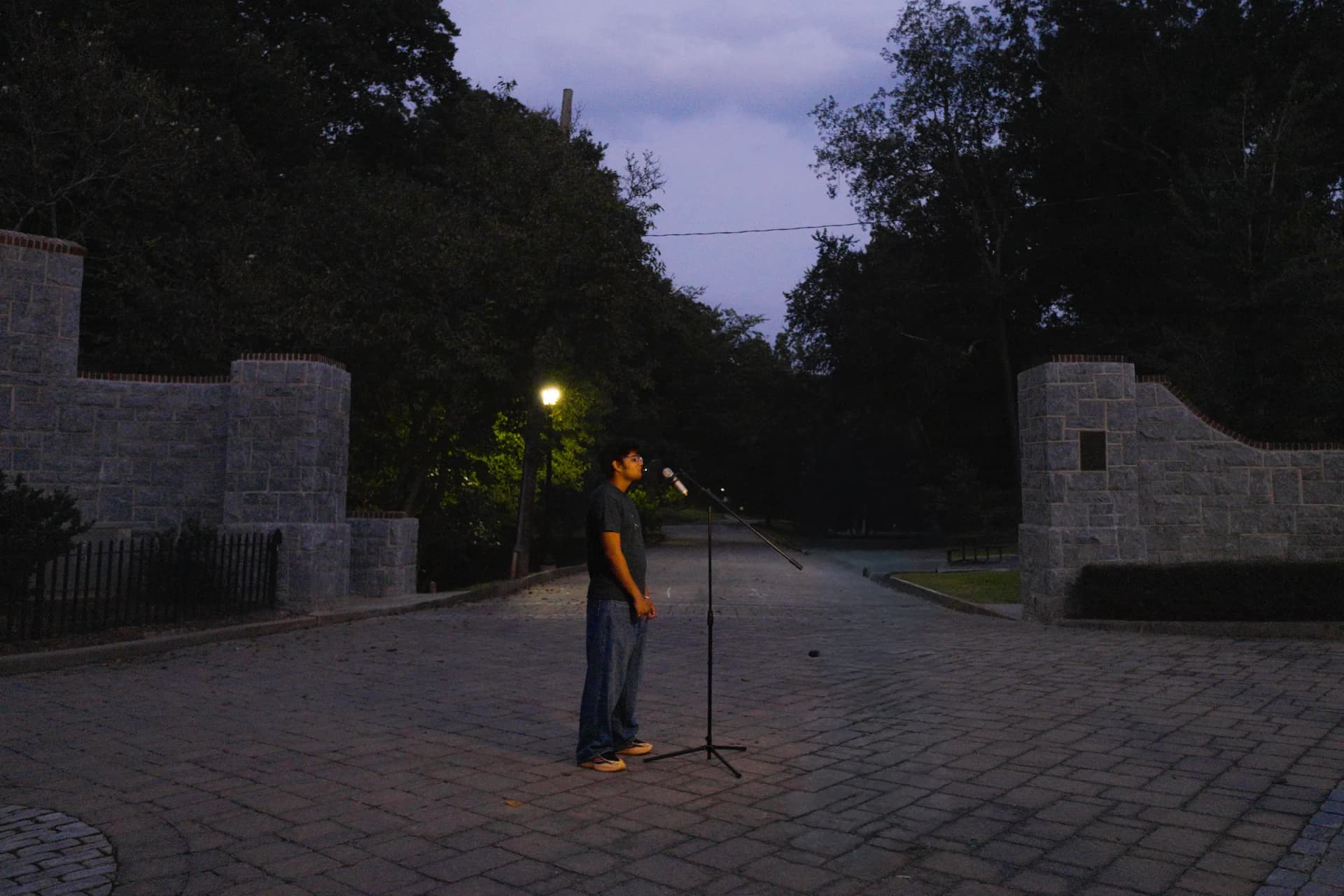 An artist alone at a microphone on a lamp-lit street at dusk